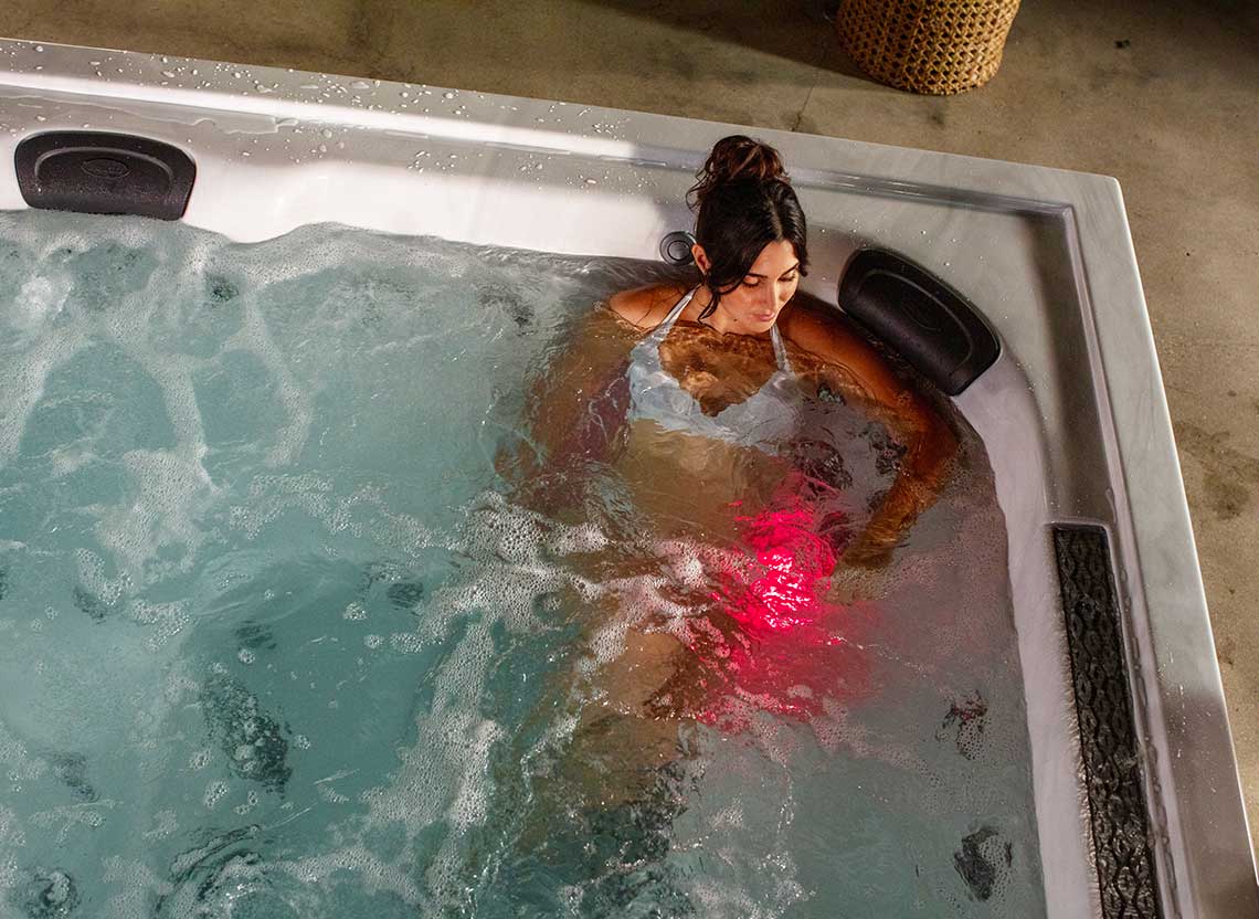 une femme se relaxe dans un spa jacuzzi j-lxl. Des jets infrarouge illuminent l'eau.
